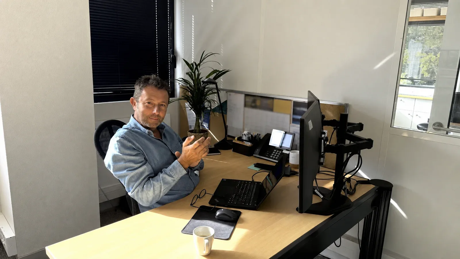 Un professionnel à son poste de travail, équipé de deux écrans et d’un téléphone